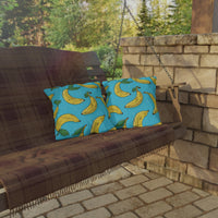 Thumbnail for Brown wooden swing with blue pillows featuring banana patterns, set against a stone wall and greenery.