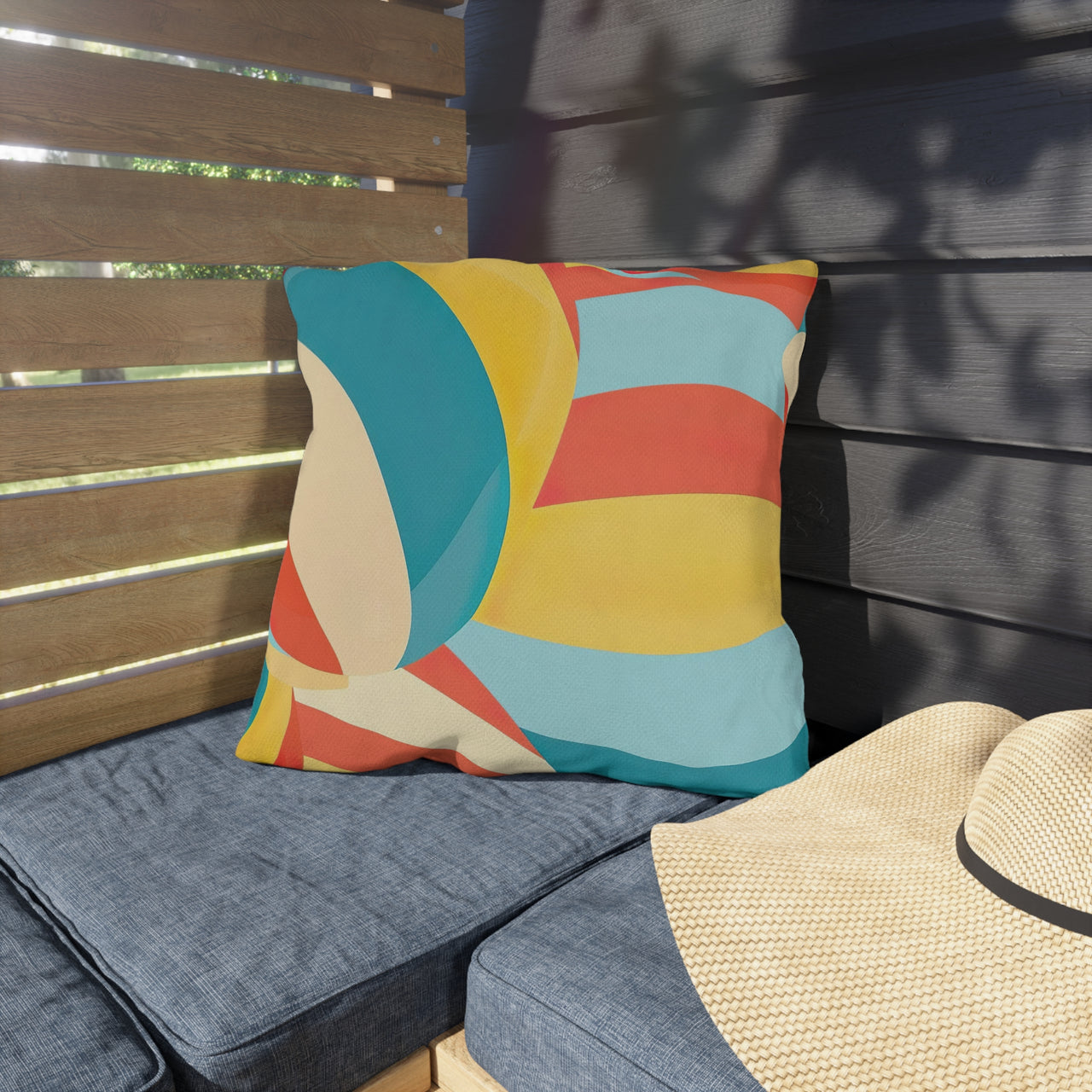 Colorful geometric pillow on a blue cushioned chair with a straw hat nearby.