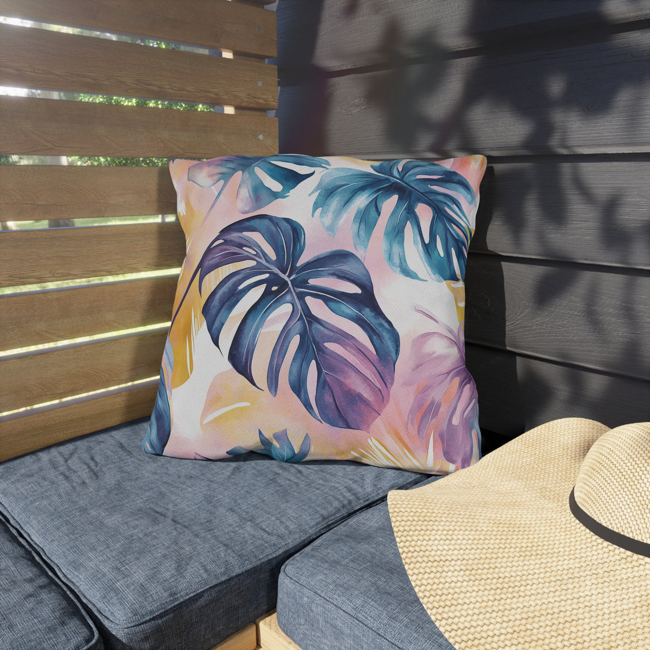 Tropical leaf patterned pillow on a gray cushioned chair with a straw hat nearby.