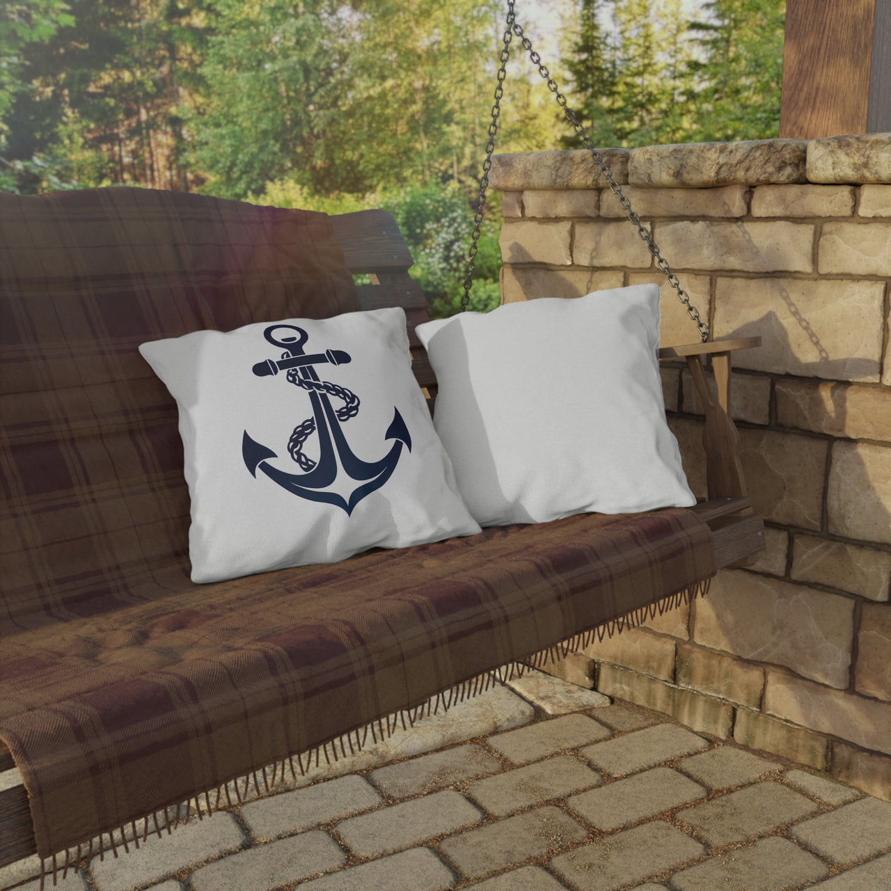 Pillow with anchor design on a wooden swing against a stone wall and greenery background