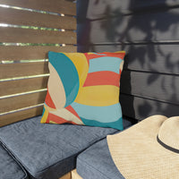 Thumbnail for Colorful geometric-patterned pillow on a gray cushioned bench with a straw hat nearby.