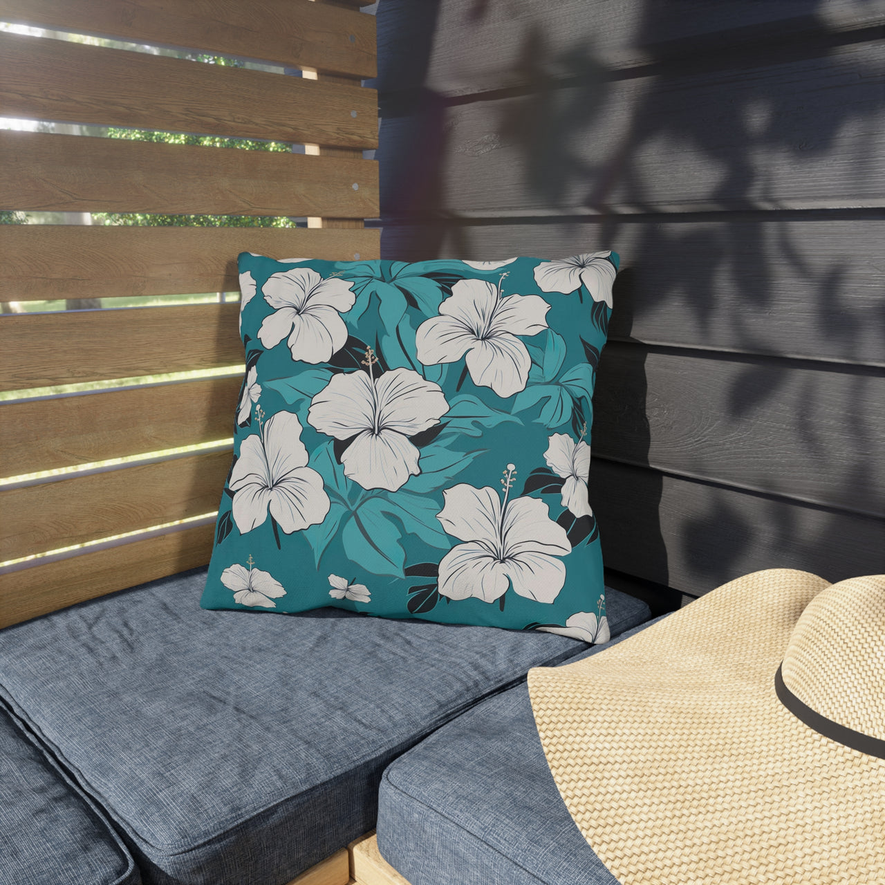 Floral-patterned pillow on a gray cushion with a straw hat nearby.