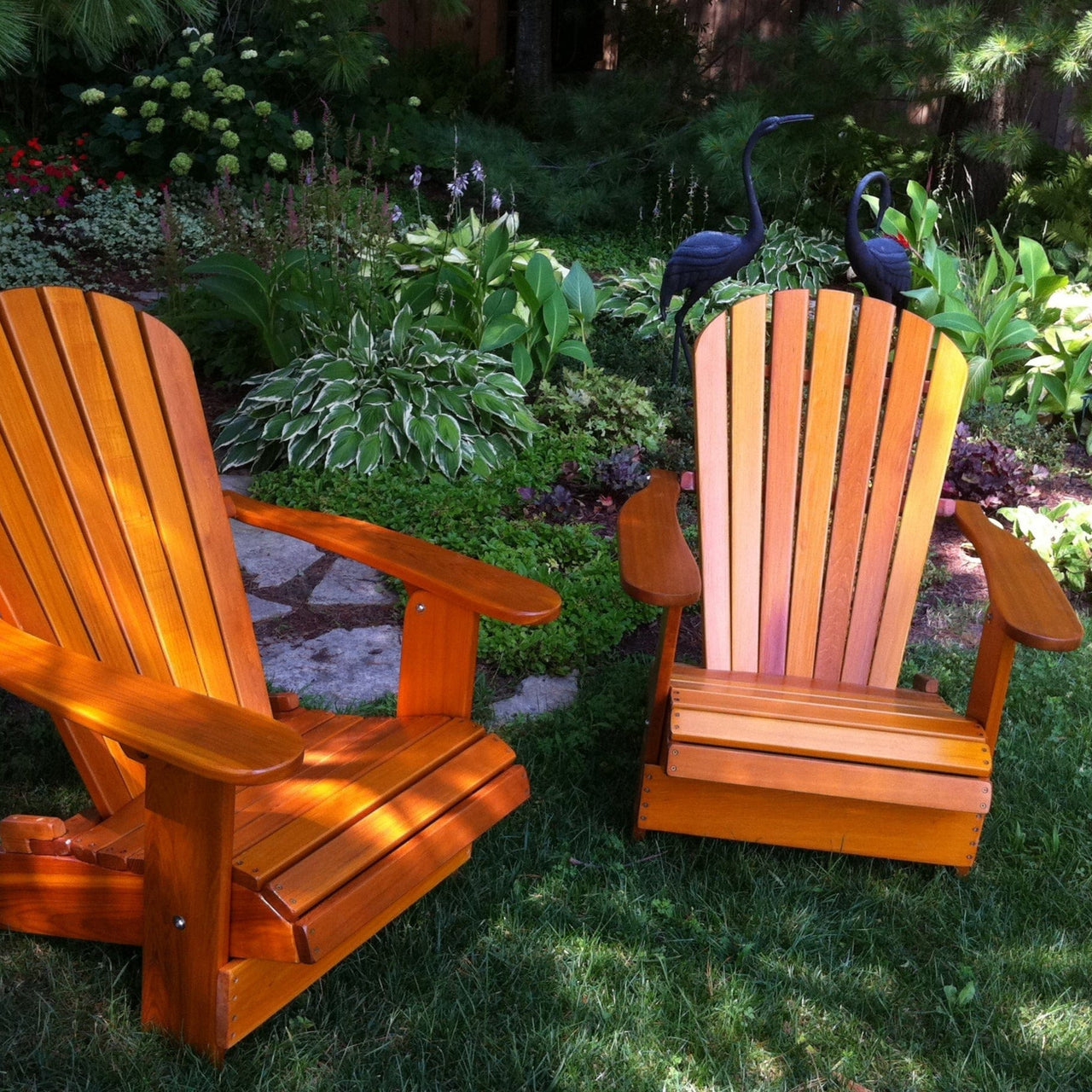 Two wooden Adirondack chairs in a garden setting with plants and birds.